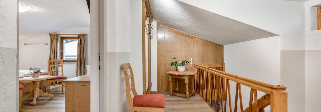 A bright, inviting hallway with wooden railing and a cozy table. The walls are painted in neutral colors, creating a warm atmosphere. - Lyns Home - Sölden
