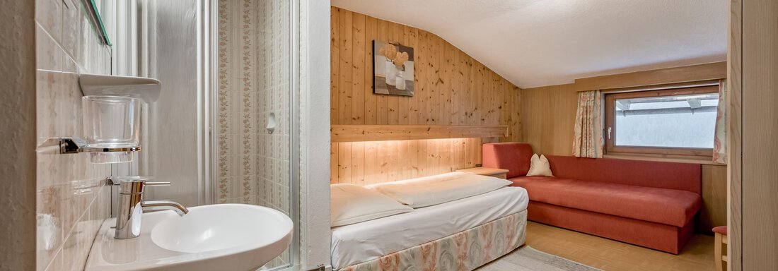 A cozy room with a bathroom area and a shower. The room features a comfortable sofa and warm wooden decor. - Lyns Home - Sölden