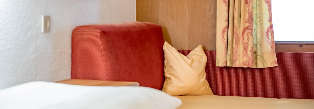 A cozy room with a red seating area and a yellow bed. A window with curtains lets in natural light. - Lyns Home - Sölden