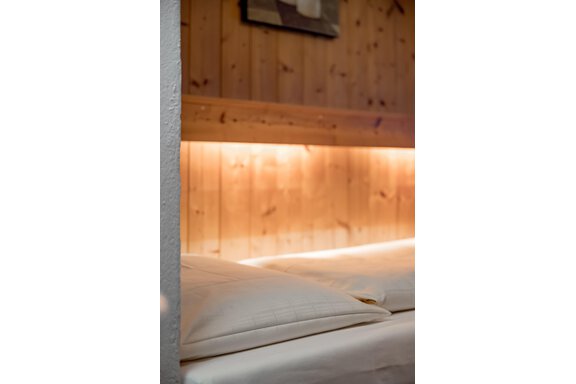 A cozy bed with white pillows in front of a wood-paneled wall. Soft light creates a relaxing atmosphere. - Lyns Home - Sölden