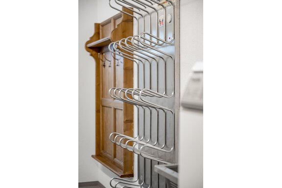 A silver clothing rack with multiple hooks stands against the wall. In the background, a wooden panel is visible. - Lyns Home - Sölden