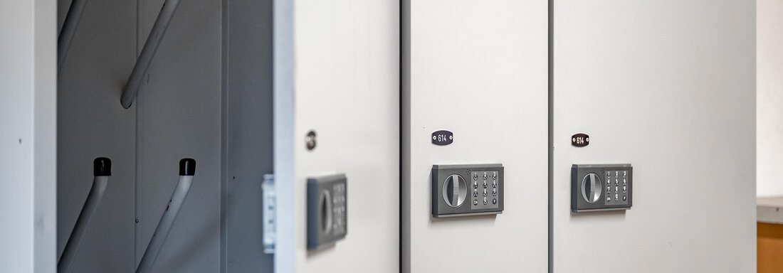 A row of white lockers with combination locks is depicted. In the background, additional elements are visible that can be used for storage. - Lyns Home - Sölden