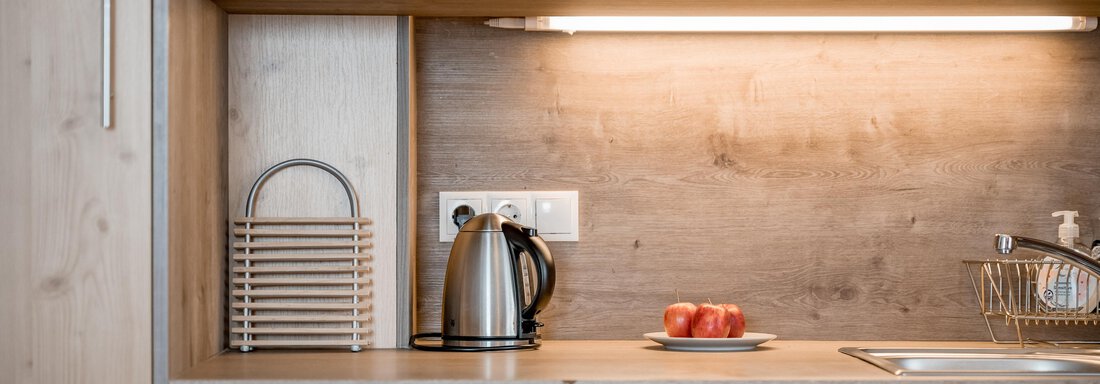 A modern kitchen unit with wooden fronts and a microwave. A kettle and apples are on the countertop. - Lyns Home - Sölden