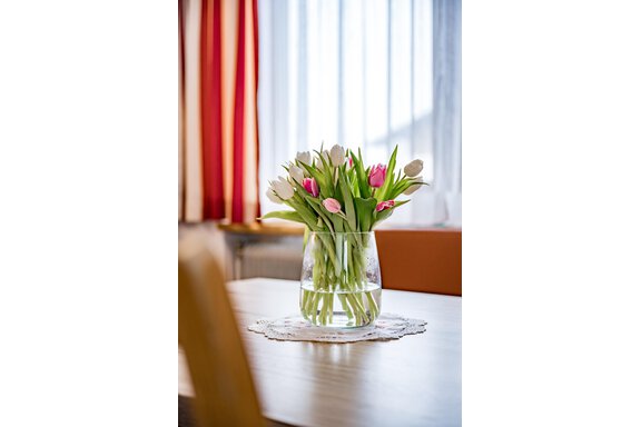 A beautiful bouquet of colorful tulips in a glass vase. The table is made of wood and there is a decorative tablecloth. - Lyns Home - Sölden