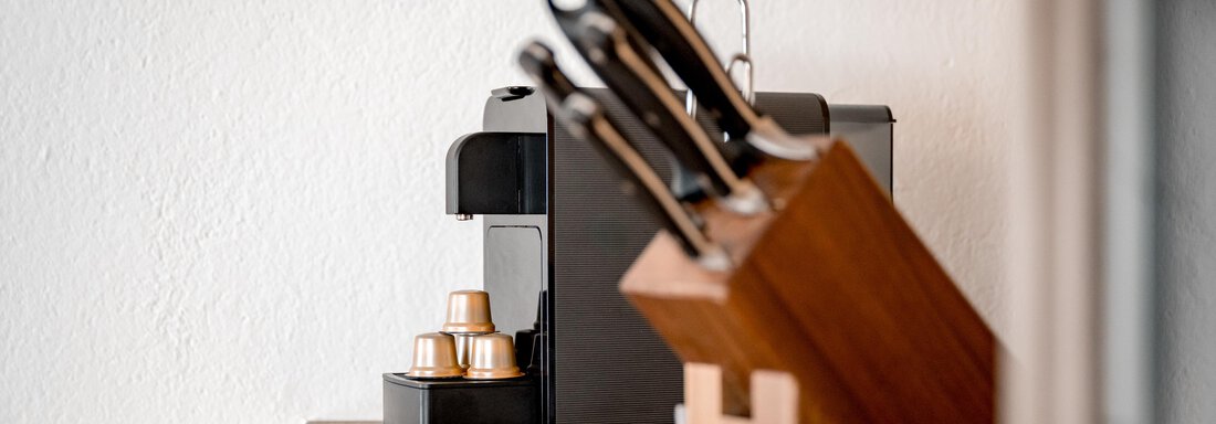 A modern coffee machine stands next to a wooden knife block. The surroundings are designed to be minimalistic and elegant. - Lyns Home - Sölden