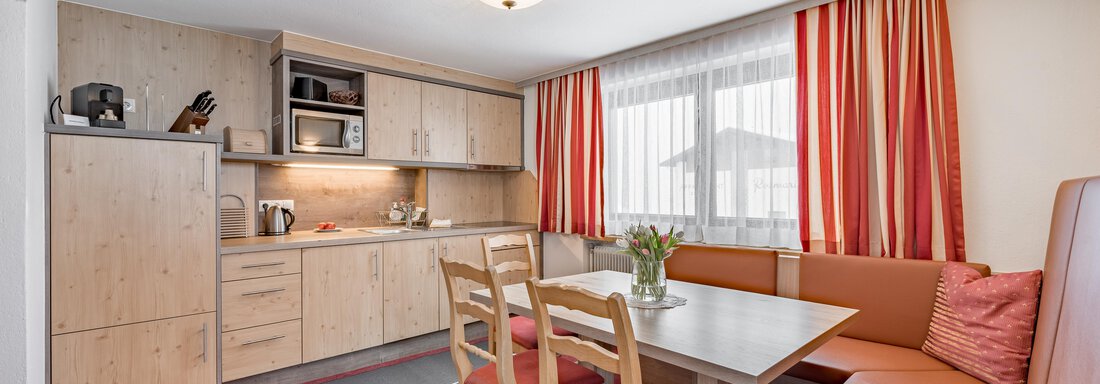 A modern kitchen with wooden cabinets and a dining area. Large windows bring a lot of light into the room. - Lyns Home - Sölden