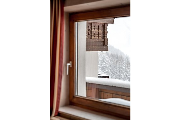 A window view of a snowy landscape. The wooden balustrade and the snow-covered trees are visible. - Lyns Home - Sölden