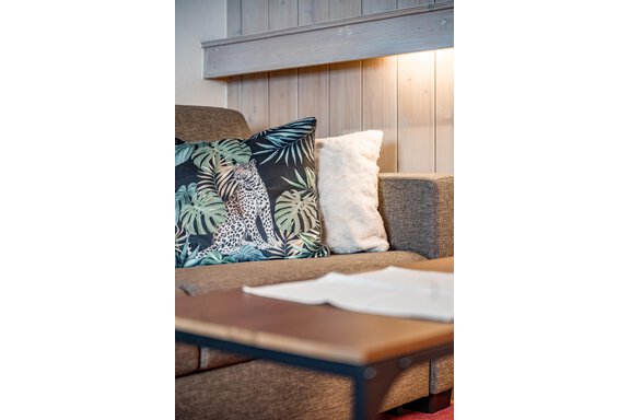 A cozy sofa with a decorative pillow featuring a plant motif. On the table, there is a small stack of paper. - Lyns Home - Sölden