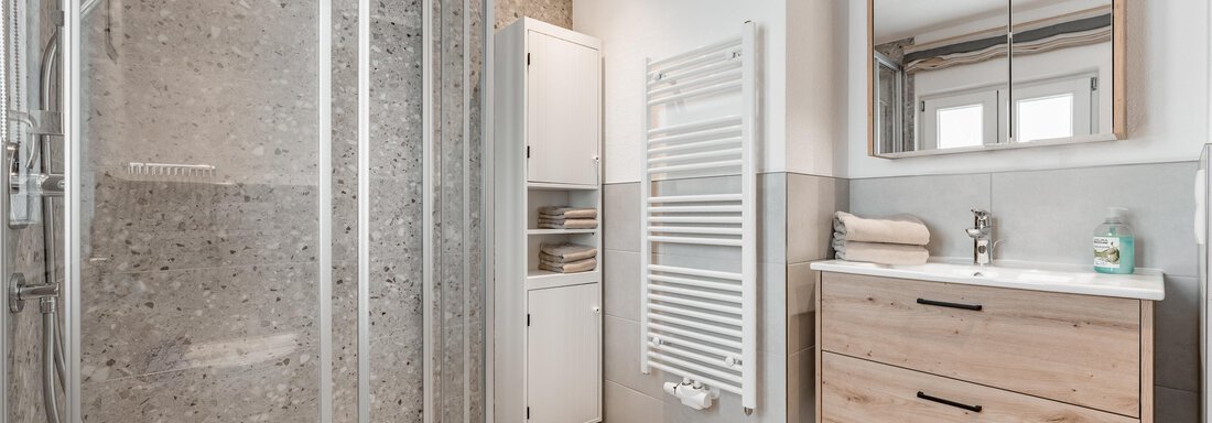 A modern bathroom with a glass shower and a wooden vanity. The walls are light and the lighting is pleasant. - Lyns Home - Sölden