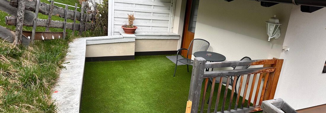 A cozy terrace with artificial grass, a table, and chairs. In the background, green meadows and part of the house are visible. - Lyns Home - Sölden