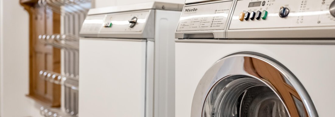 A modern laundry room with a washing machine and a dryer. In the background, there is a wooden clothes dryer. - Lyns Home - Sölden
