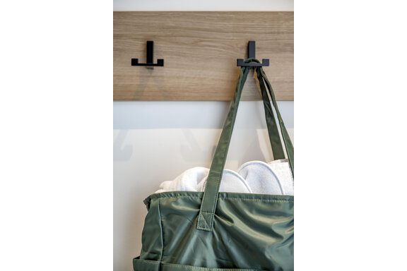 A green bag hangs on a wooden sign with black hooks. Inside the bag are white towels. - Marco's Mountain Home - Sölden