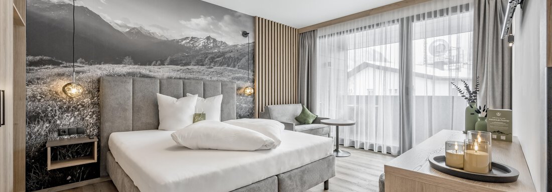 A modern hotel room with a double bed and a large window. The walls are decorated with an impressive mountain picture. - Marco's Mountain Home - Sölden