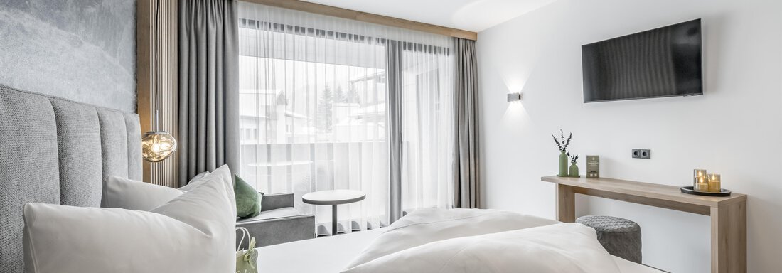 A modern hotel room with a large bed and elegant pillows. There are windows with curtains, a television, and a small sitting area. - Marco's Mountain Home - Sölden