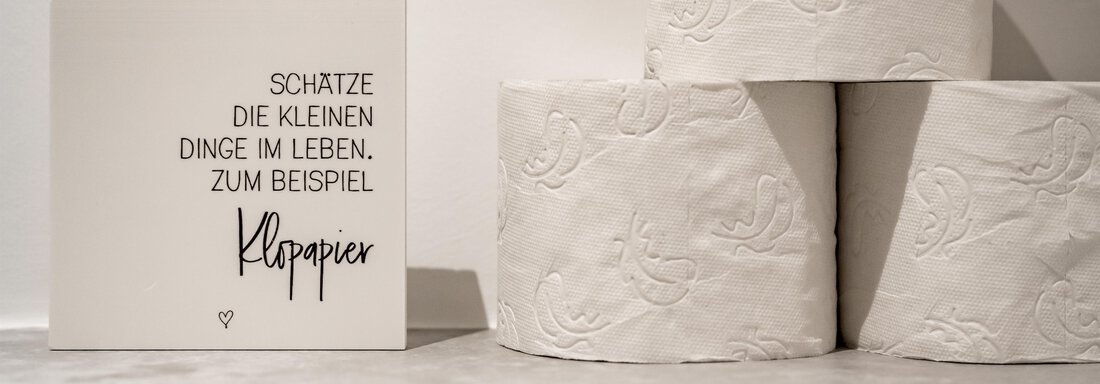 A white sign with black text stands next to a roll of toilet paper. The saying encourages appreciating the little things in life. - Marco's Mountain Home - Sölden