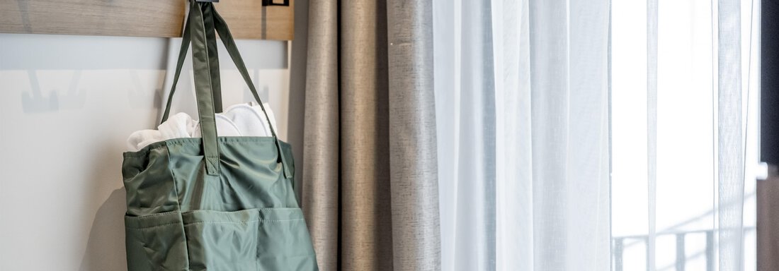A green bag hangs on a wooden shelf with hooks. In the background, you can see a curtain and a lot of natural light. - Marco's Mountain Home - Sölden