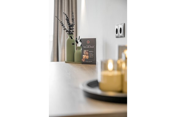 A modern table with a green vase filled with decorative branches. Next to the vase is a menu and a group of candles. - Marco's Mountain Home - Sölden