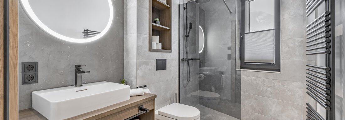 A modern bathroom with an elegant shower and a large mirror. The walls are in neutral gray tones and there are wooden details. - Marco's Mountain Home - Sölden