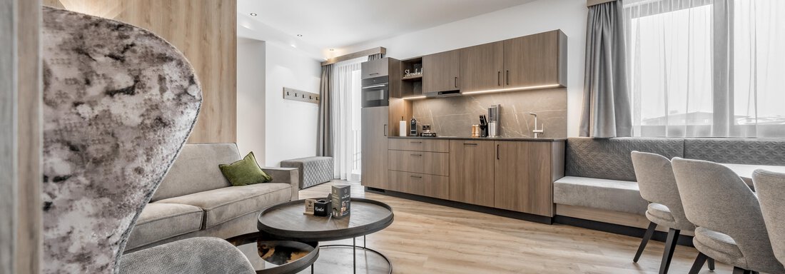 A modern living space with an elegant couch and a round table. The kitchen is designed in neutral colors and offers plenty of storage space. - Marco's Mountain Home - Sölden