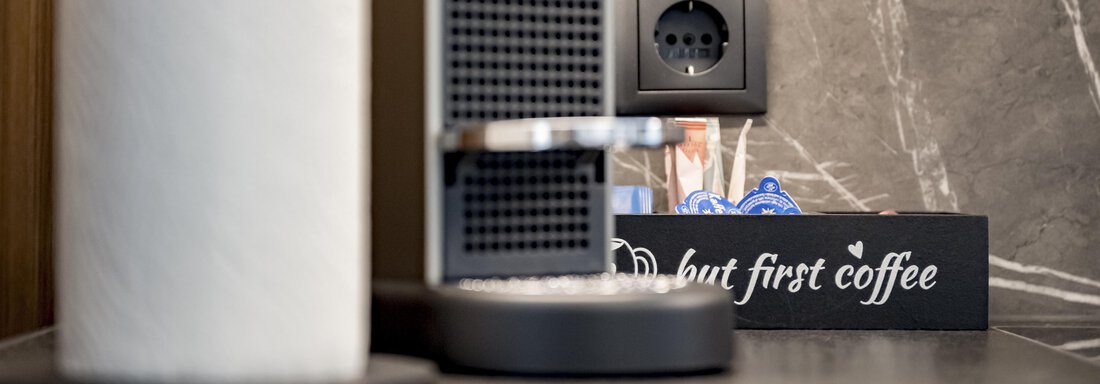 A modern coffee station with a coffee capsule machine and a stylish storage for paper towels. In the background, there is a sign with the saying "Do but first coffee." - Marco's Mountain Home - Sölden