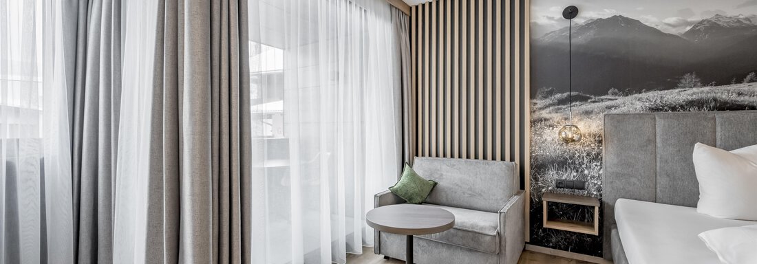 A modern hotel room with a comfortable sofa and a small table.  
Large windows let in plenty of light and offer a view of a landscape with mountains. - Marco's Mountain Home - Sölden