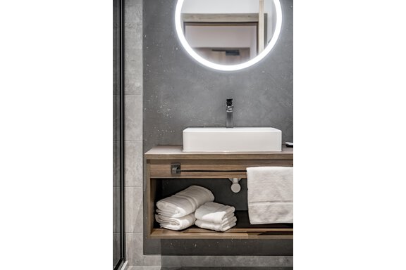 A modern bathroom with an elegant sink and a round mirror. Clean towels are neatly placed on the shelf underneath. - Marco's Mountain Home - Sölden