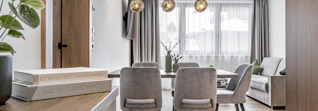 A modern living room with a bright ambiance. The room is furnished with a sofa, a dining table, and stylish pendant lights. - Marco's Mountain Home - Sölden