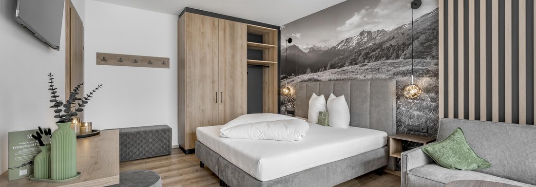 A modern hotel room with a large bed and a bright, inviting decor. On the wall, there is a large picture of the mountains, giving the room a special touch. - Marco's Mountain Home - Sölden
