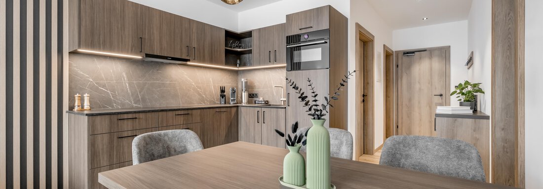 A modern and bright kitchen with wooden shelves and elegant pendant lights. The dining table is made of wood and decorated with green decorative elements. - Marco's Mountain Home - Sölden