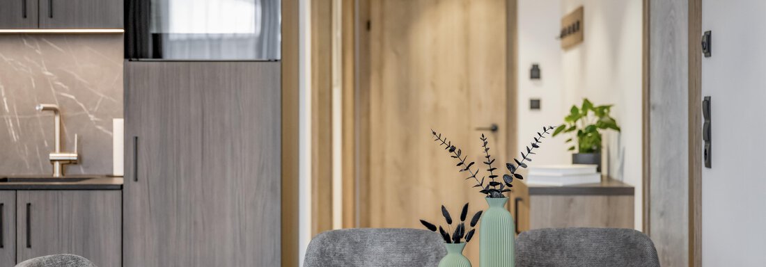 A modern dining area with a wooden table and gray chairs. Stylish lamps hang above the table, and there are decorative elements like vases and plants. - Marco's Mountain Home - Sölden