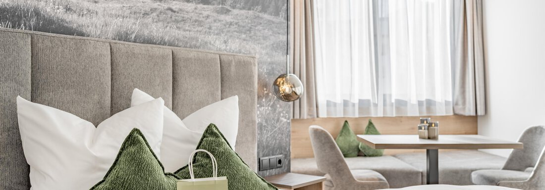 A modern hotel room with a cozy bed and decorative pillows. There is a table with chairs by the window, and a mountain landscape is depicted on the wall. - Marco's Mountain Home - Sölden