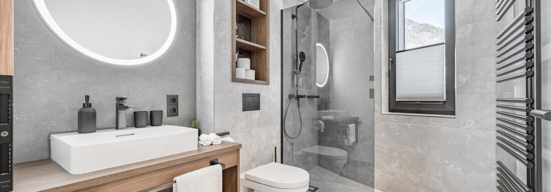 A modern bathroom with a large shower and elegant surfaces. A round mirror and wooden shelves add a stylish touch to the space. - Marco's Mountain Home - Sölden