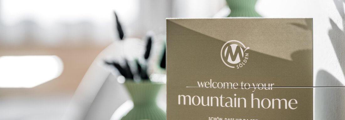 A welcome card for a chalet in the mountains is on a table. In the background, a green vase and some pens can be seen. - Marco's Mountain Home - Sölden