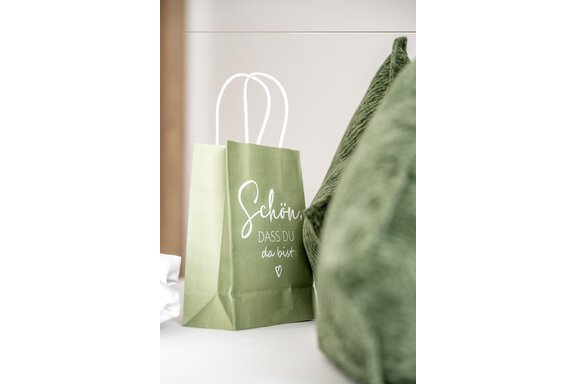 A green paper bag with the inscription "Nice to have you here" stands next to a soft, green cushion. The foreground colors are soft and inviting. - Marco's Mountain Home - Sölden