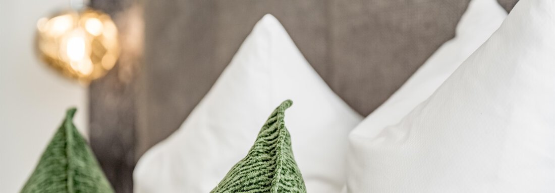 A cozy bedroom with green and white cushions. In the background, a warm light source is visible. - Marco's Mountain Home - Sölden