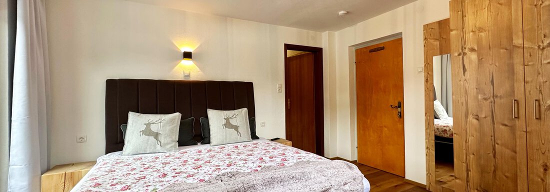 A cozy bedroom with a large bed and decorative pillows. The room has wooden floors and warm lighting. - Mountain Lodge Sölden - Sölden