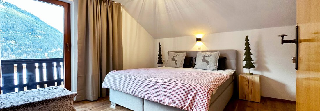 A cozy bedroom with a large bed and modern furniture. A window offers a view of the mountains and the wooden floor creates a warm atmosphere. - Mountain Lodge Sölden - Sölden