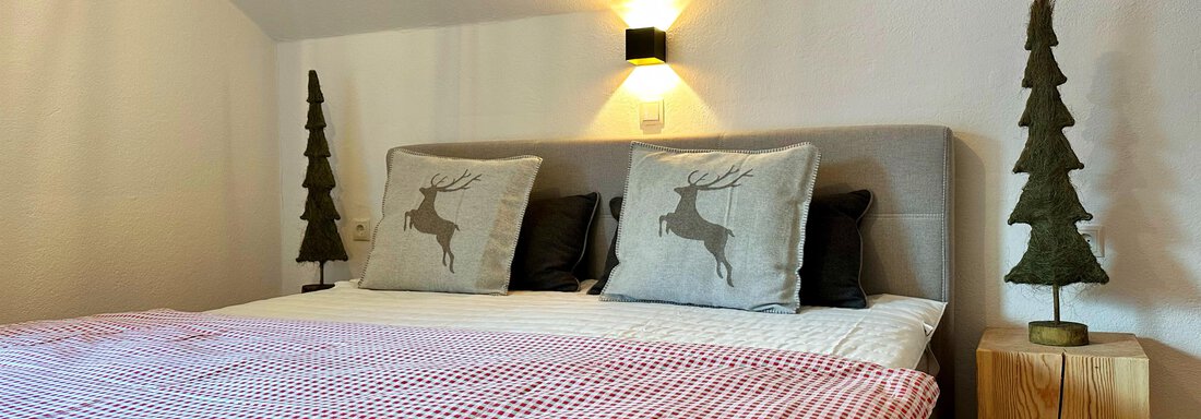 A cozy bedroom with a large bed and decorative pillows. Next to the bed are two small wooden trees. - Mountain Lodge Sölden - Sölden