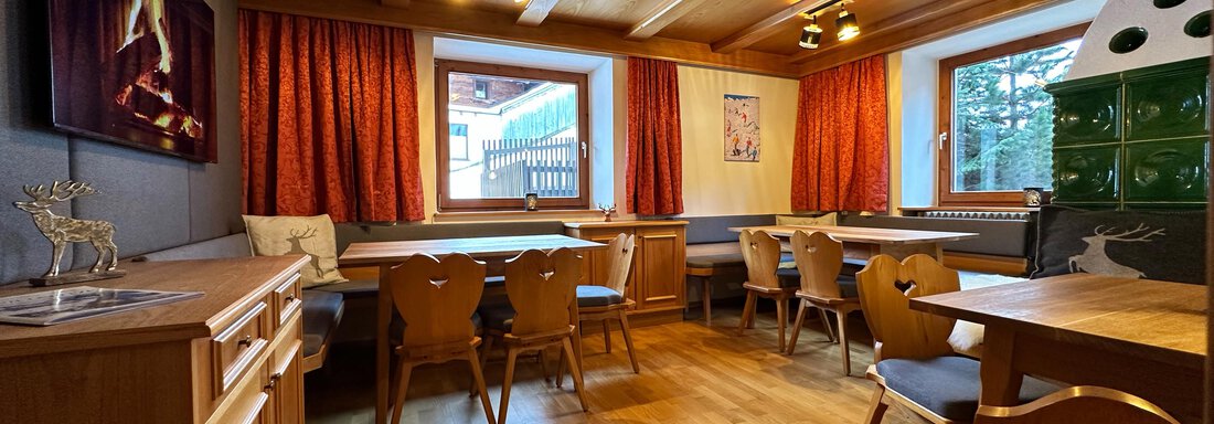 A cozy room with wood paneling, tables, and chairs. Red curtains and a window create a comfortable atmosphere. - Mountain Lodge Sölden - Sölden