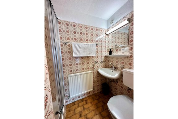 A small, modern bathroom with a floral tile pattern and a towel over the sink. The furnishings include a sink, a toilet, and a shower stall. - Mountain Lodge Sölden - Sölden