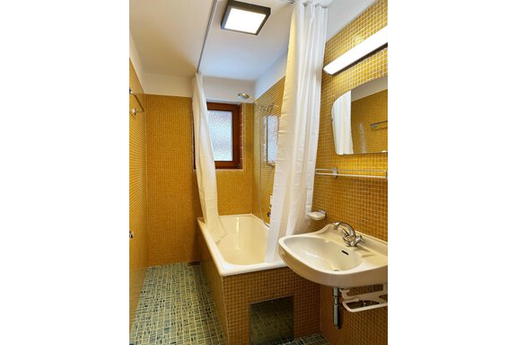 A simple bathroom with a bathtub and shower curtain. The walls are tiled in a warm yellow tone. - Mountain Lodge Sölden - Sölden