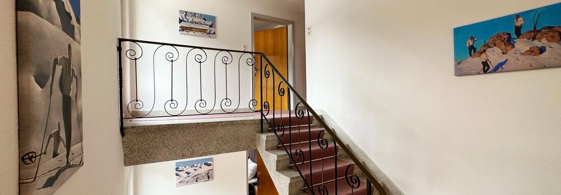 A bright stairway area with a curved staircase and decorative pictures on the walls. The walls are kept in neutral colors, creating an inviting atmosphere. - Mountain Lodge Sölden - Sölden