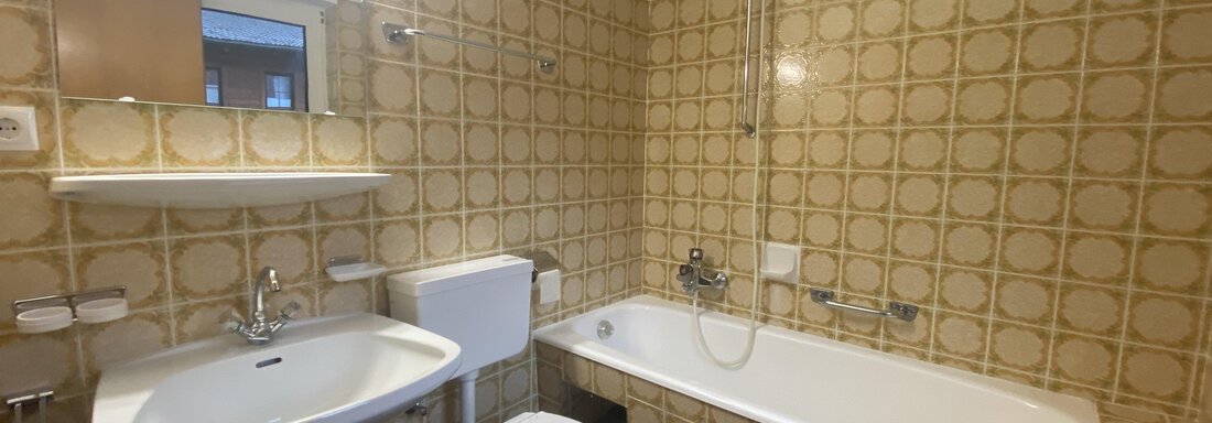 A bathroom with a bathtub, a sink, and a toilet. The walls are tiled in a vintage pattern. - Mountain Lodge Sölden - Sölden