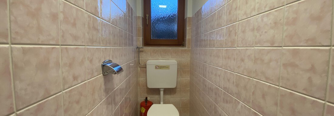 A small, clean toilet with pink tiles. In the background, a window and a fire extinguisher can be seen. - Mountain Lodge Sölden - Sölden