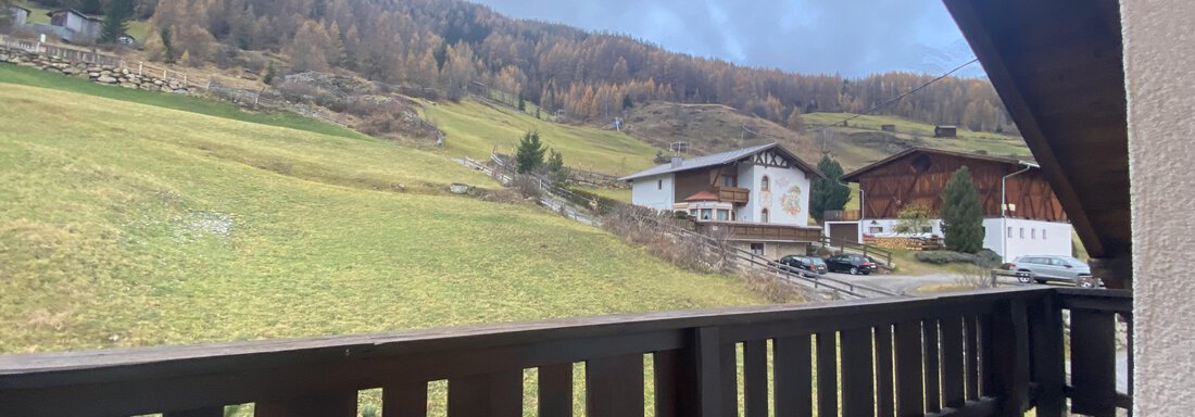 A picturesque landscape with green meadows and typical alpine houses. In the background, gentle hills and forested mountains can be seen. - Mountain Lodge Sölden - Sölden