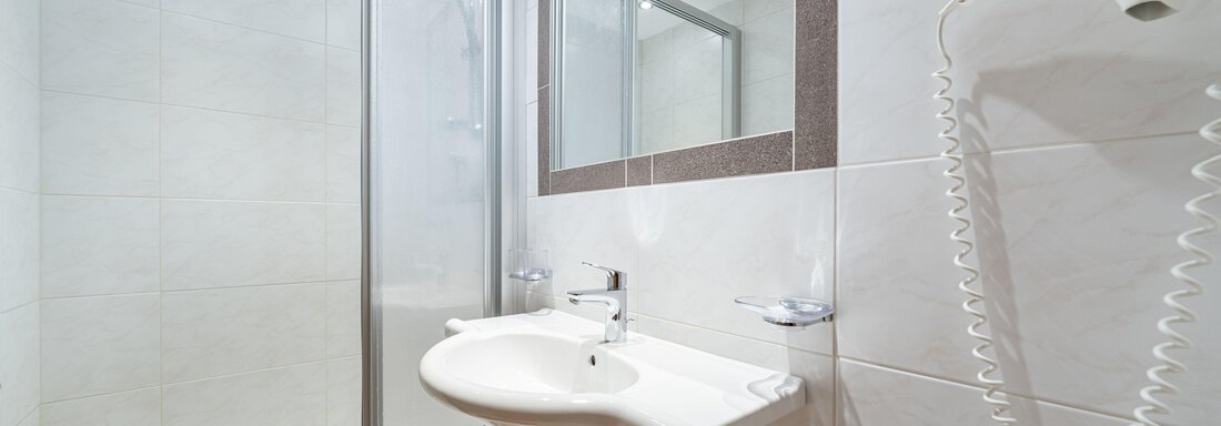 A modern bathroom with a shower and a sink. The walls are light-colored tiled and the ambiance feels clean and tidy. - Pension Birkenheim - Sölden