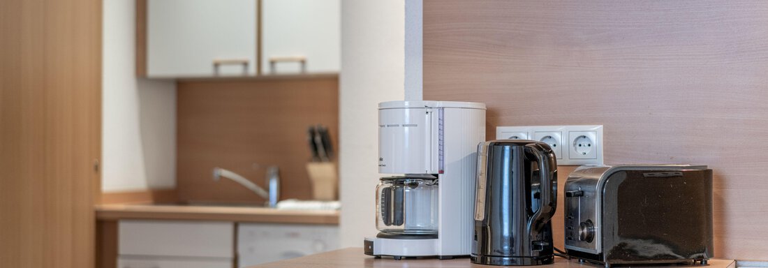 A modern kitchen with wood surfaces. On the counter are a coffee machine, a kettle, and a toaster. - Pension Birkenheim - Sölden