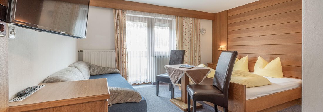 A cozy room with a sofa, a table, and chairs. A large window provides plenty of daylight. - Pension Birkenheim - Sölden