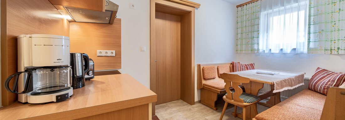 A modern kitchen with a dining area and cozy seating. Daylight through the window creates a friendly atmosphere. - Pension Birkenheim - Sölden