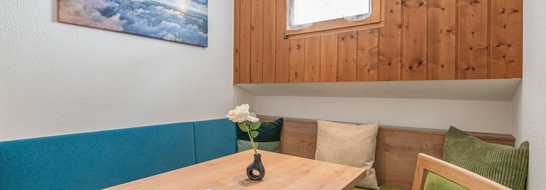 A cozy dining area with a green bench and a wooden table. A picture of clouds and mountains hangs on the wall. - Pension Birkenheim - Sölden